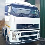 White Volvo FM 400 6x4 truck tractor front view with stone guard mesh and yellow safety stripe parked in yard